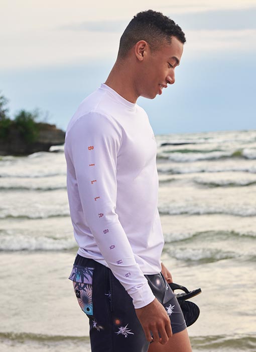 Homme qui marche sur la plage et qui porte un rashguard billabong blanc