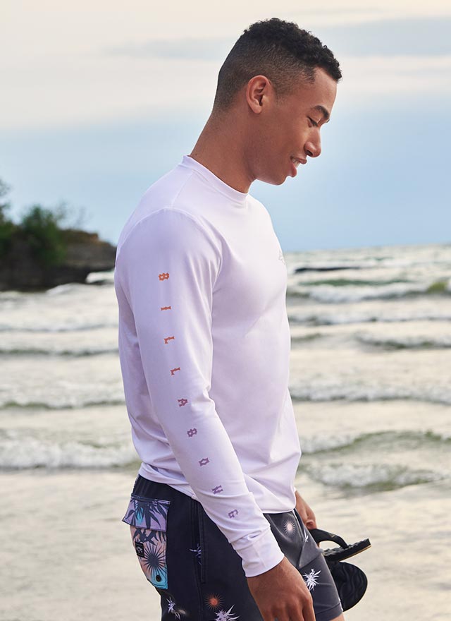 Homme qui marche sur la plage et qui porte un rashguard billabong blanc